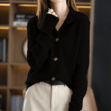 Femme portant un cardigan noir élégant avec boutons, manches longues, posant devant une étagère. Mode automne-hiver, style chic et décontracté.